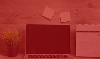 Zu sehen sind ein Laptop auf einem Schreibtisch mit einem Notizblock und Post-ist an der Wand