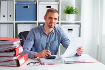 Ein Manager hält ein Blatt Papier in der Hand und tippt etwas in einen Taschenrechner