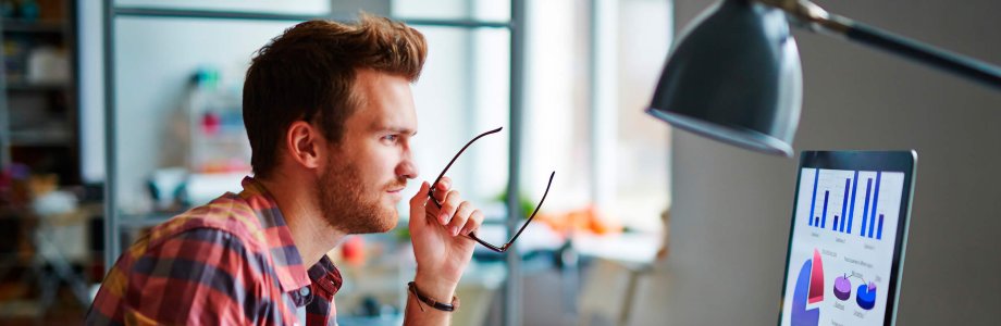 Ein Mann sieht sich Grafiken auf einem Computer an und hält seine Brille in der Hand