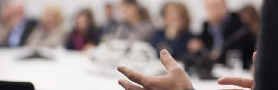 Hände eines Dozenten mit Seminarteilnehmern im Hintergrund