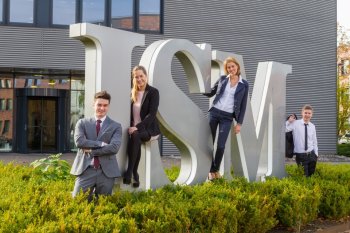 Menschen stehen vor einer Figur aus Buchstaben, die die Abkürzung ISM ergeben