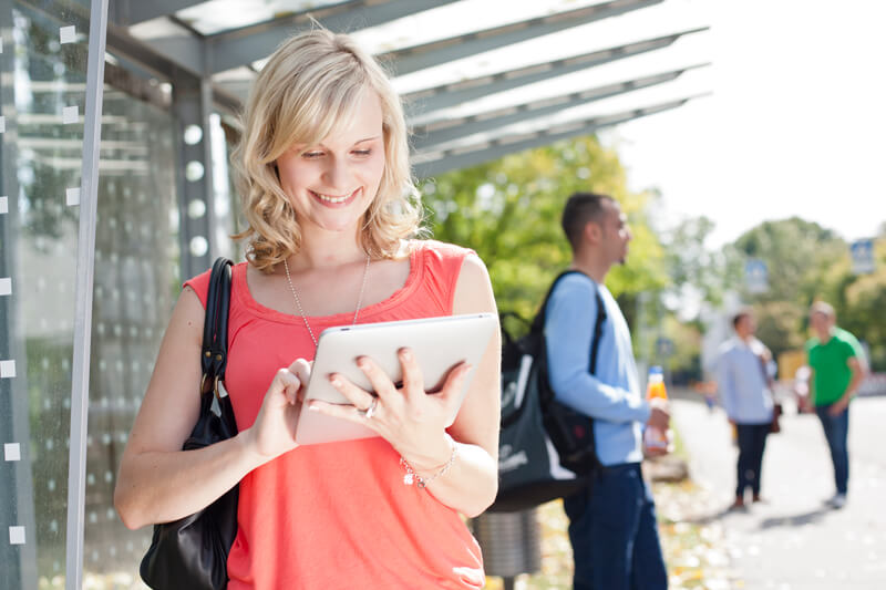 Frau steht vor einer Fachhochschule und bedient ein Tablet